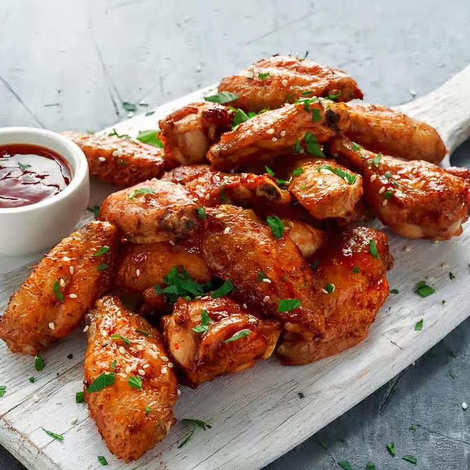 Glazed chicken wings with sesame seeds and parsley, served with a side of dipping sauce.