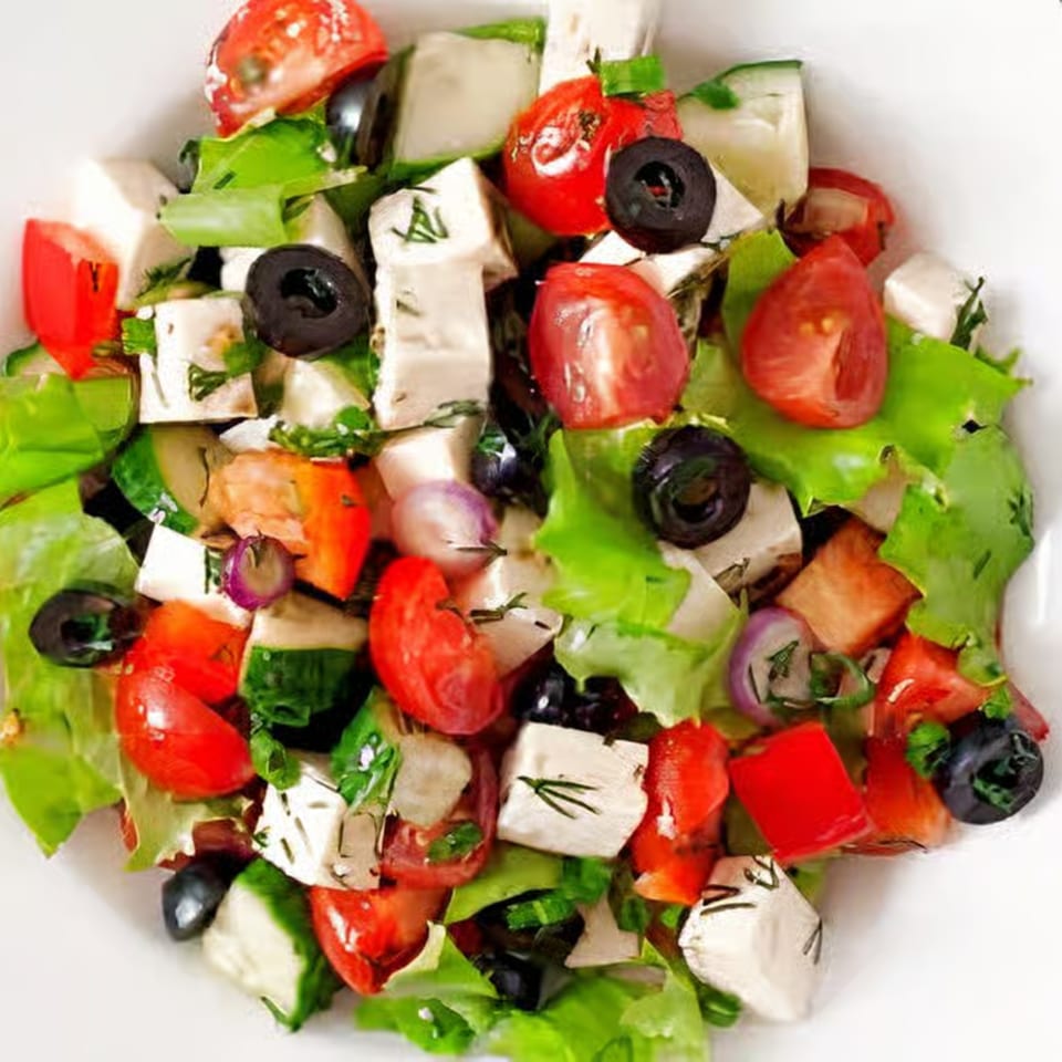 Close-up of a vibrant Greek salad with feta, olives, tomatoes, and lettuce in a white bowl.