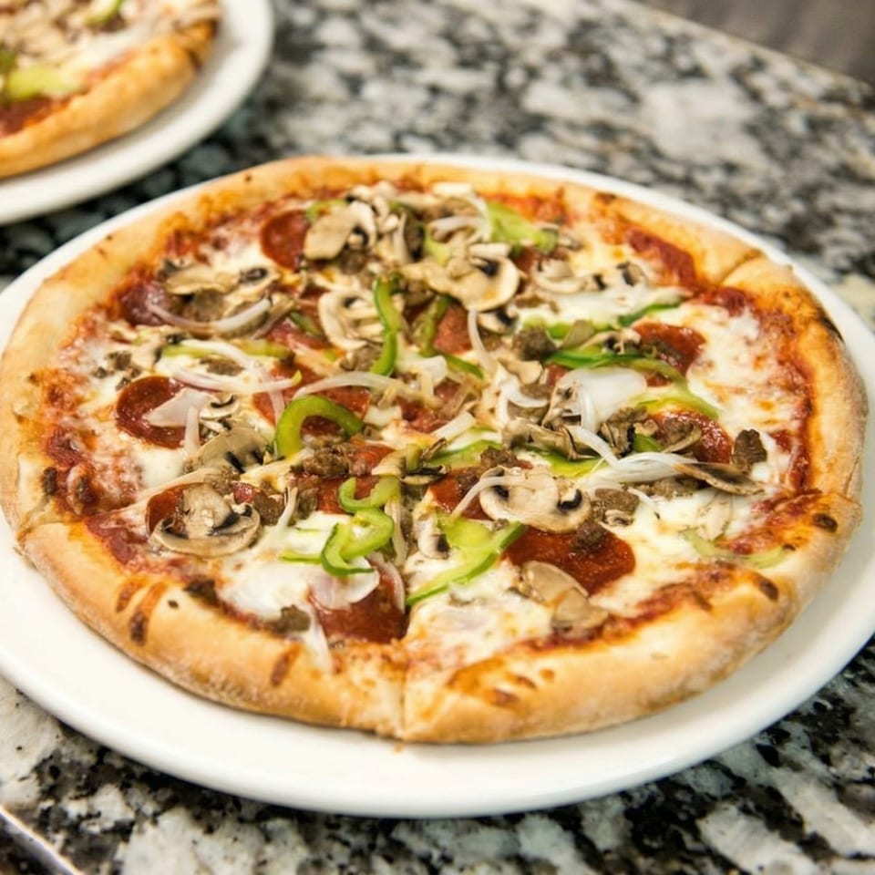 A whole pizza with pepperoni, mushrooms, green peppers, and onions on a white plate.