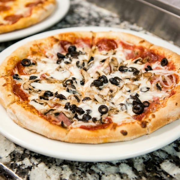 A freshly baked pizza with mushrooms, black olives, pepperoni, and onions on a white plate.