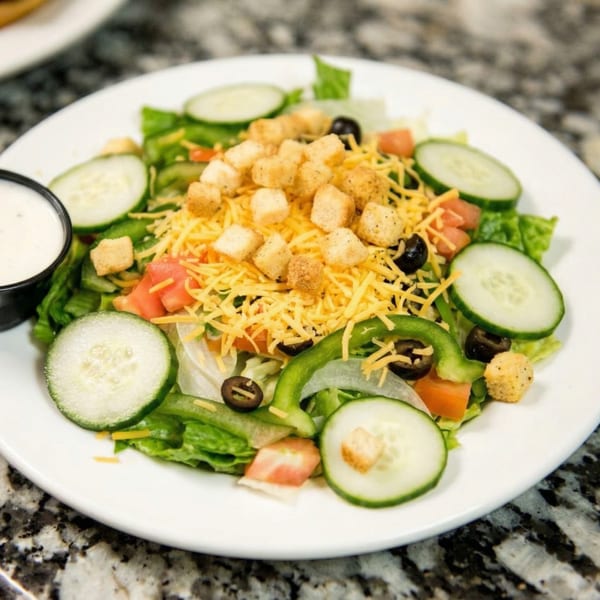 Fresh garden salad with lettuce, cucumbers, tomatoes, olives, shredded cheese, and croutons, with a side of ranch.